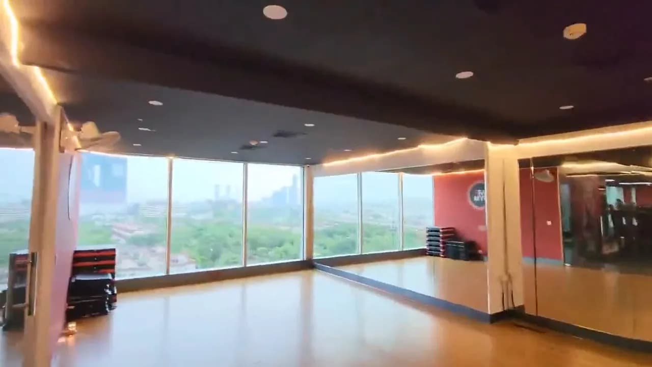 An empty gym studio with a wooden floor, a mirror wall and floor-to-ceiling windows over the city
